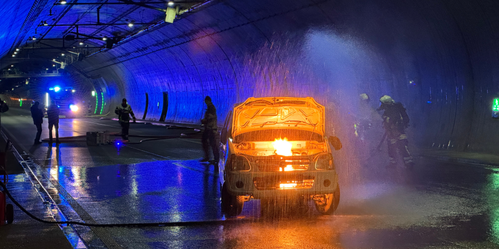 Ein Auto brennt im Tunnel. Feuerwehrleute löschen es.