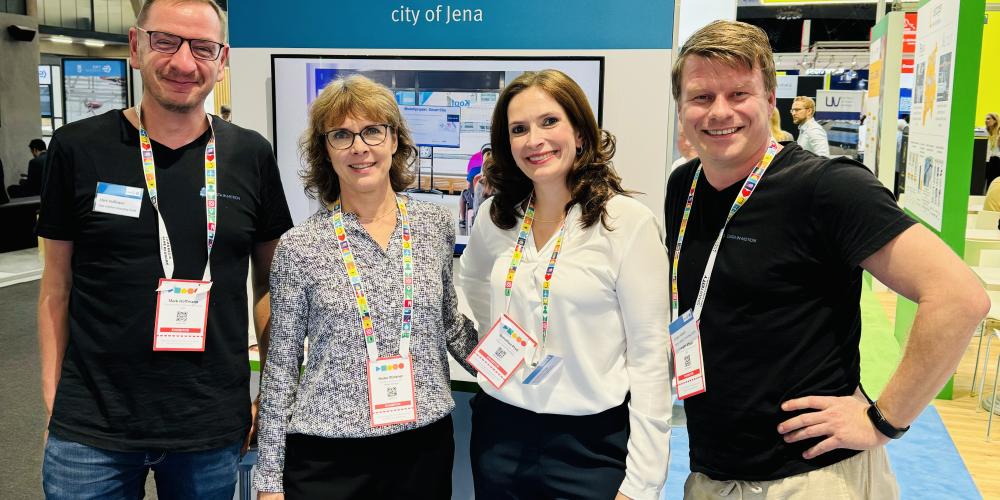 Vier Personen stehen vor einem Messestand und lächeln in die Kamera.