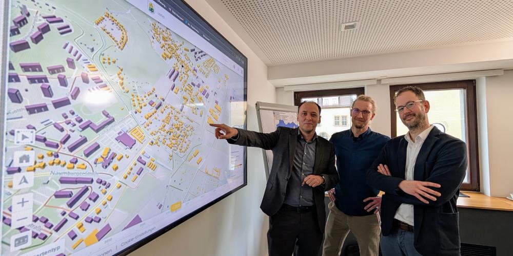 Christian Gerlitz, Bürgermeister und Dezernent für Stadtentwicklung und Umwelt der Stadt Jena, Kevin Muschalle-Momberg Klimaschutzkoordinator der Stadt Jena, und Christian Dornack, Bereichsleiter Strategie bei den Stadtwerken Jena Netze stehen vor einer Karte der Kommunalen Wärmeplanung.