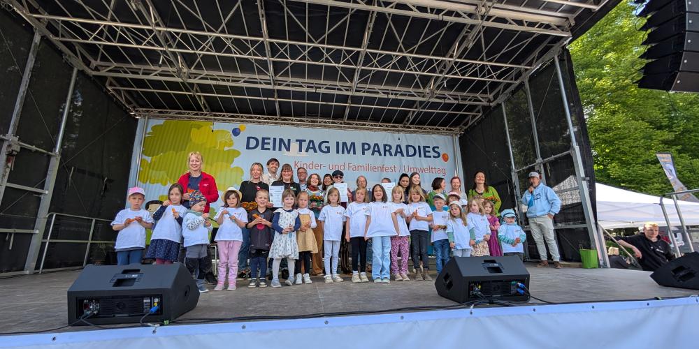 Auf einer Bühne stehen eine Reihe von Kindern und Jugendliche plus einige Erwachsene.