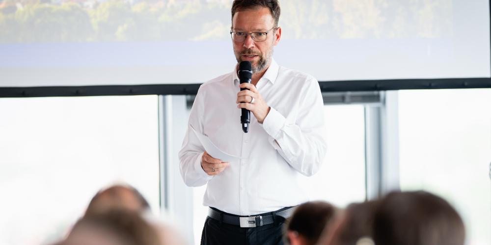 Ein Mann steht vor einem Publikum und spricht in ein Mikrofon.