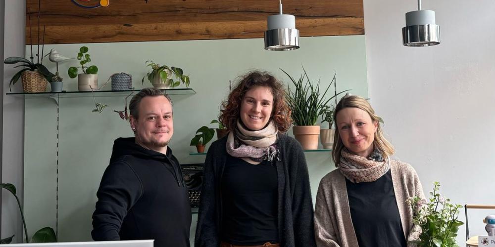 Ein Mann und zwei Frauen stehen hinter einer Empfangstheke. Dahinter hängt ein Bild mit der Aufschrift ProbierLaden.