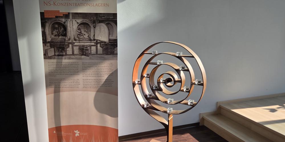 Eine Informationsstele informiert über die NS-Zeit. Daneben steht ein Kerzenständer mit mehreren Teelichtern.