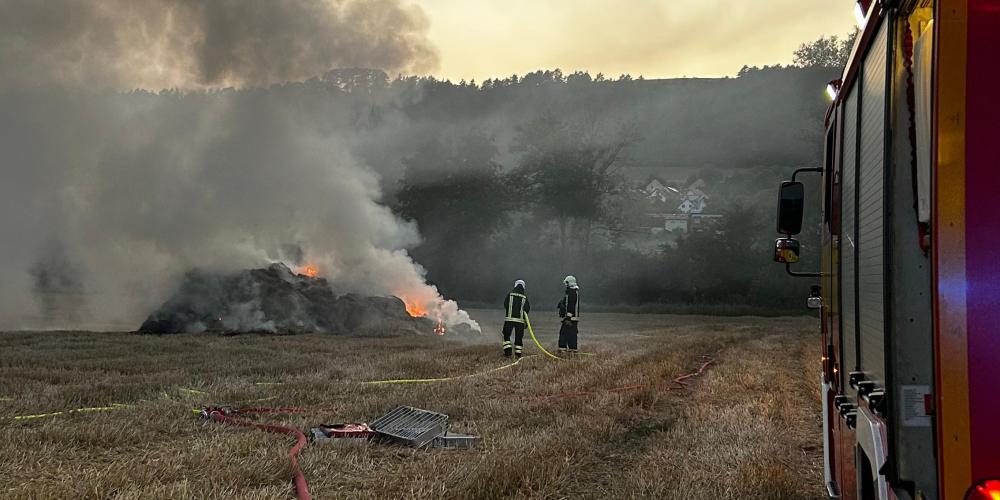 Feuerwehrauto auf einem Feld mit starkem Rauch und brennenden Strohballen