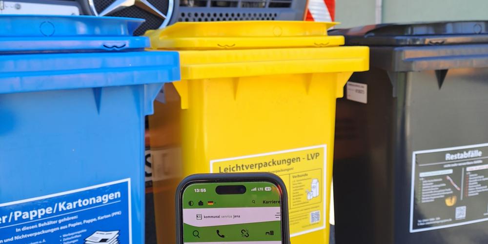 Handy mit abgebildeten Behälter-Konfigurator vor einer blaueb, gelben und scharzen Mülltonne sowie einem Müllfahrzeug