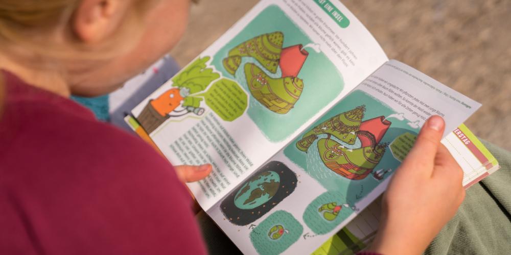 Kind schaut sich Heft mit bunten Seiten an.