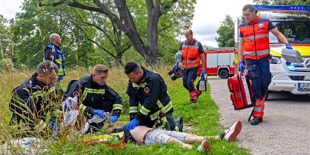 Feuerwehr und Notarztteam eilen zu einer still liegenden Person am Boden.