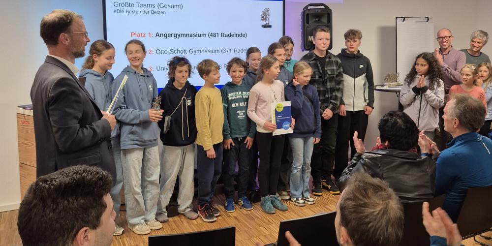 Der Oberbürgermeister steht mit einer Gruppe vor Schülern vor Publikum. Eine Schülerin hält eine Urkunde, eine andere einen Pokal.