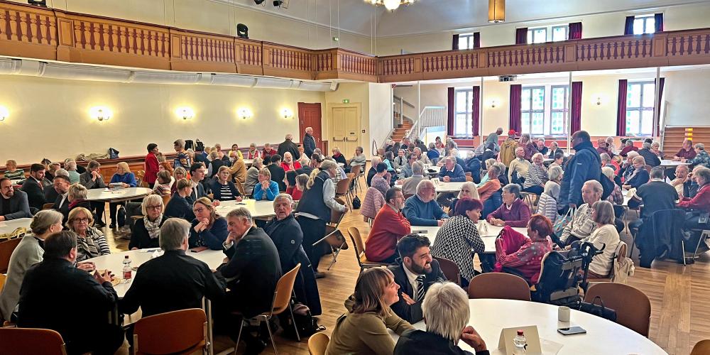 Menschen sitzen an Runden Tischen in einem großen Saal