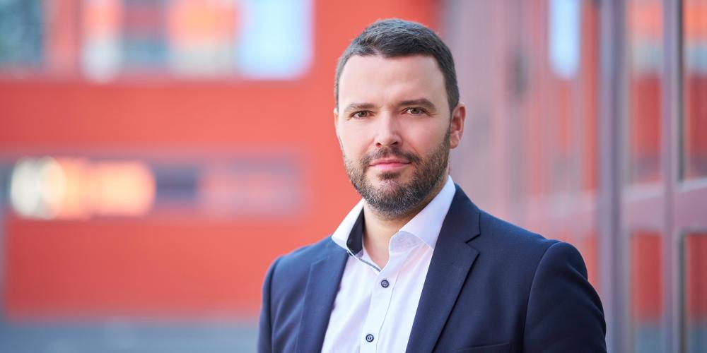 Mann in blauem Anzug steht im Außenbereich und lächelt