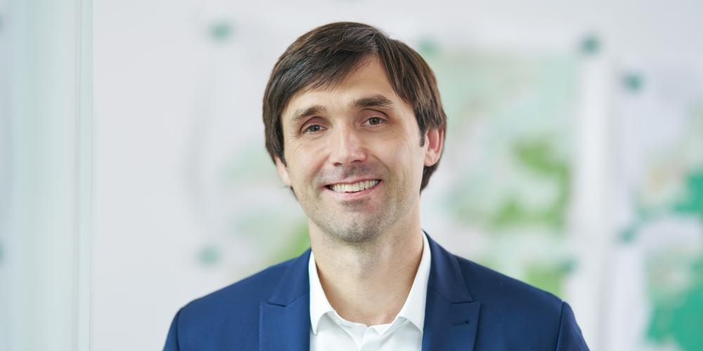 Mann in blauem Anzug steht in einem Raum und lächelt