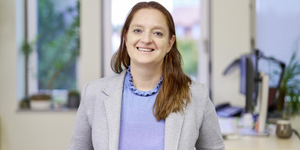 Frau sitzt an einem Tisch und lächelt in die Kamera