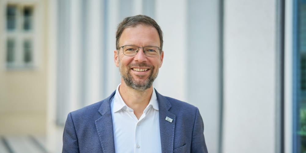 Mann in blauem Anzug steht im Außenbereich und lächelt