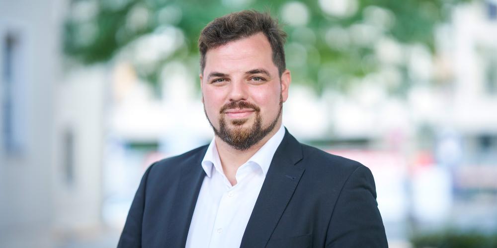 Mann in blauem Anzug steht im Außenbereich und lächelt