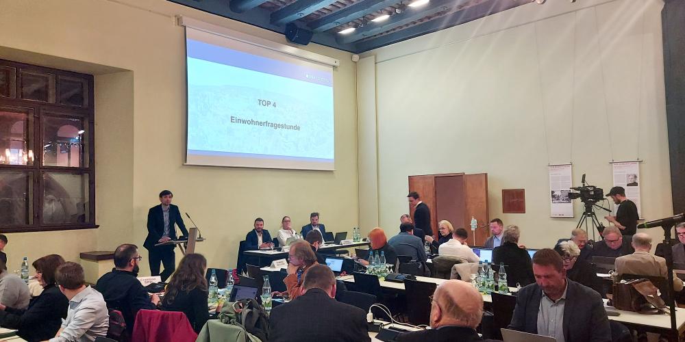 Stadtratsmitglieder sitzen an Tischen im Historischen Rathaus, ein Redner steht am Rednerpult