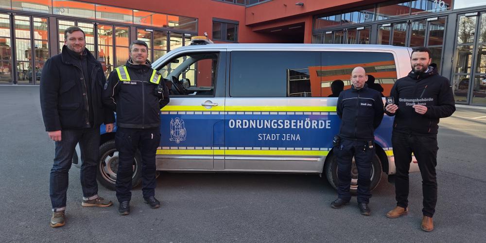 Vier Männer stehen vor einem Auto der Ordnungsbehörde und sehen in die Kamera.