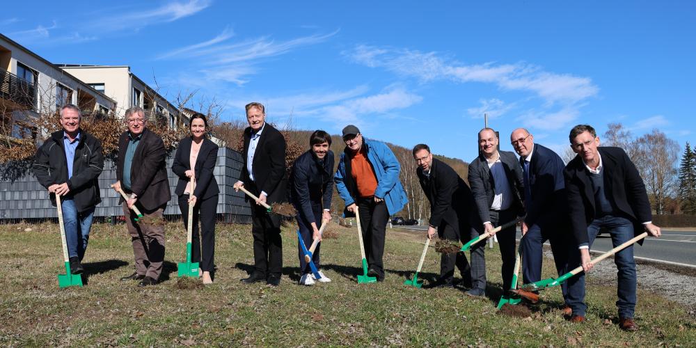 8 Männer und eine Frau stehen in einer Reihe mit einem Spaten bzw. Spitzhacke in der Hand für einen symbolischen Spatenstich.
