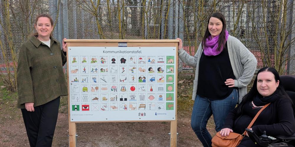 Kathleen Lützkendorf (Dezernentin für Soziales, Gesundheit, Zuwanderung und Klima),  Daniela Egert (Einreicherin des Vorschlags) und Ines Muskalla (Beauftragte für Menschen mit Behinderung der Stadt Jena) bei der Spielplatztafel im Marienwäldchen.