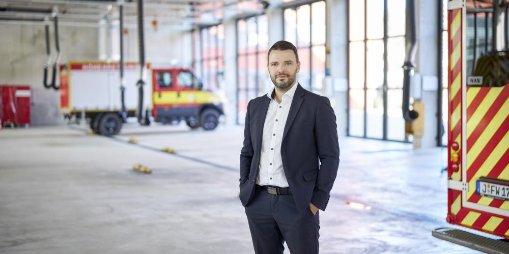 Bürgermeister Benjamin Koppe schaut in der Fahrzeughalle der Feuerwehr die Kamera.
