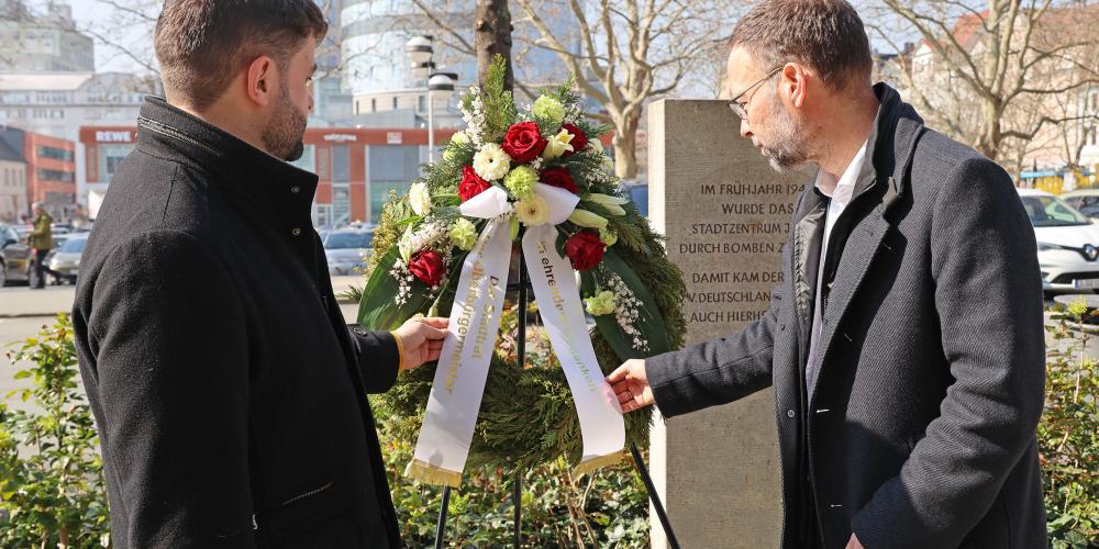 Zwei Personen stehen an einem Gedenkkranz