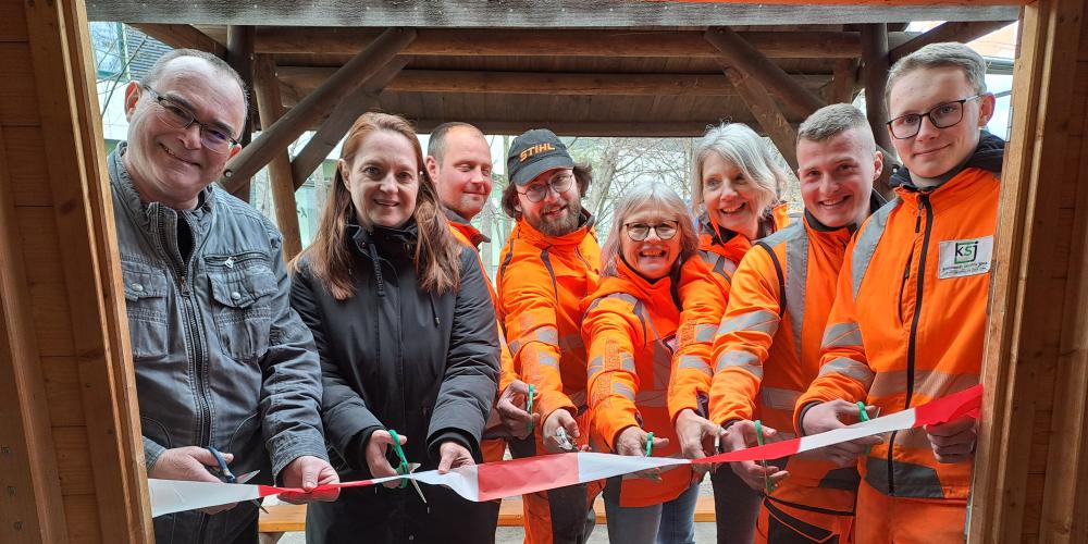 Acht Männer und Frauen schneiden ein Band durch.