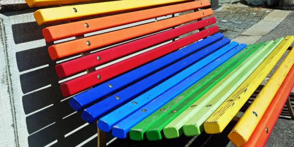 Eine Parkbank, die regenbogenfarben gestrichen ist.