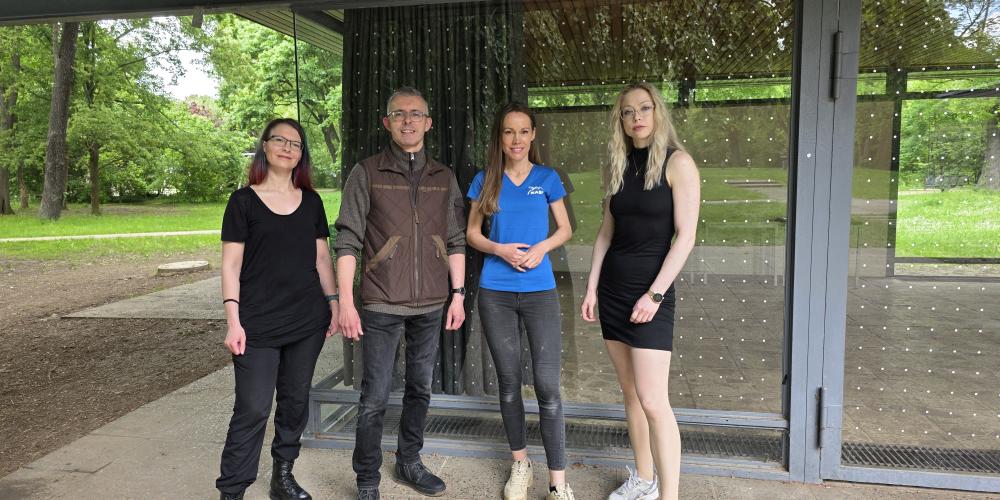 Ein Mann und drei Frauen stehen vor einer Glasfront, die mit Punktfolie gegen Vogelschlag beklebt ist.
