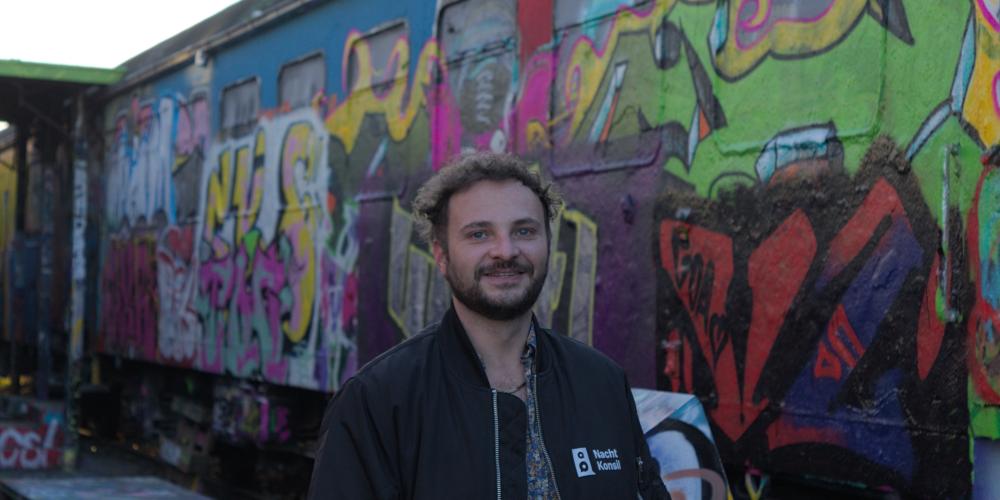 Ein Mann steht vor einer Mauer, auf der Graffiti aufgesprüht sind