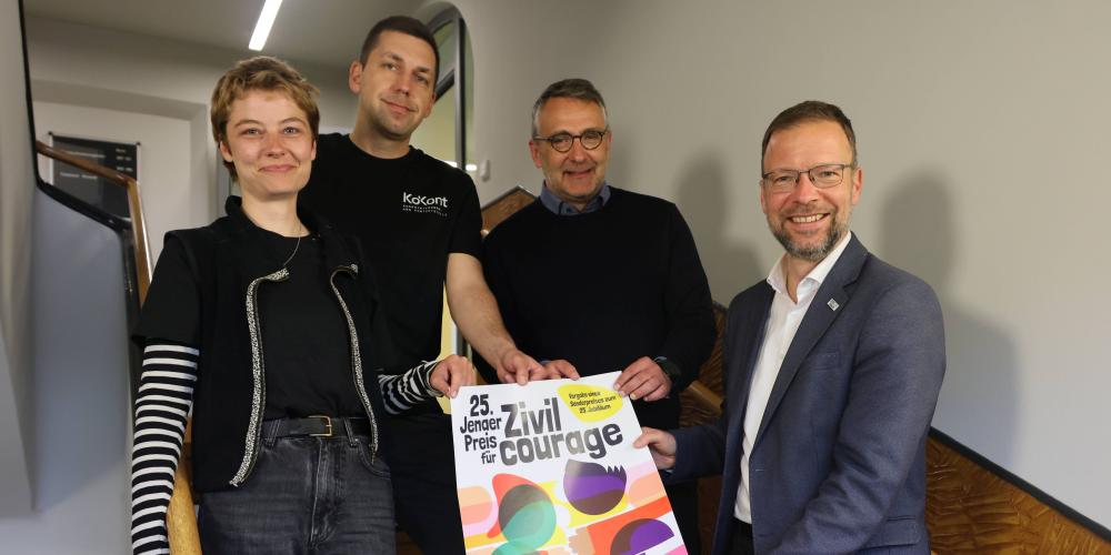 Vier Menschen halten im Treppenhaus ein Plakat.