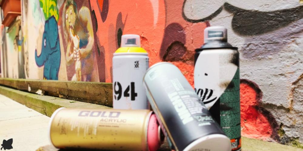 Vier Spraydosen vor einer besprühten Wand