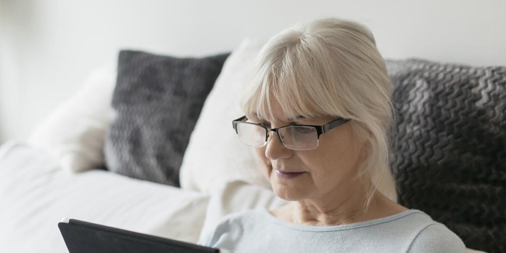 Seniorin sitzt auf einer Couch und surft mit einem Tablet