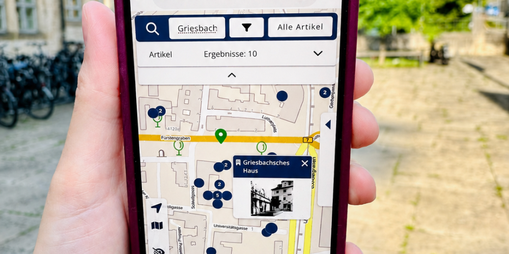 Hand hält Smartphone, auf dem eine Stadtkarte zu sehen ist. 