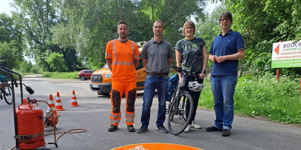 Drei Männer und eine Frau mit Fahrrad stehen hinter einer runden Markierung auf der Straße.