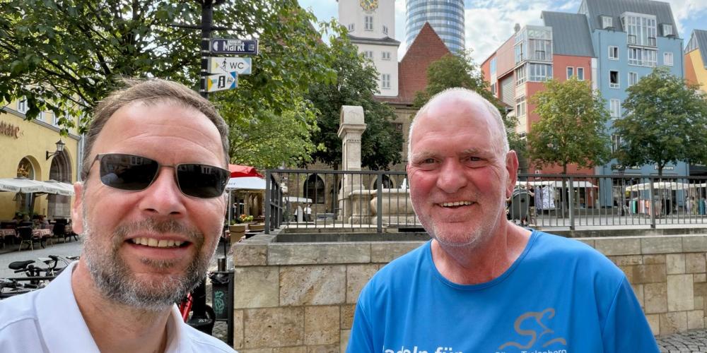 Zwei Männer stehen auf dem Markt in Jena und machen ein Slfie mit Rathaus und Jentower im Hintergrund