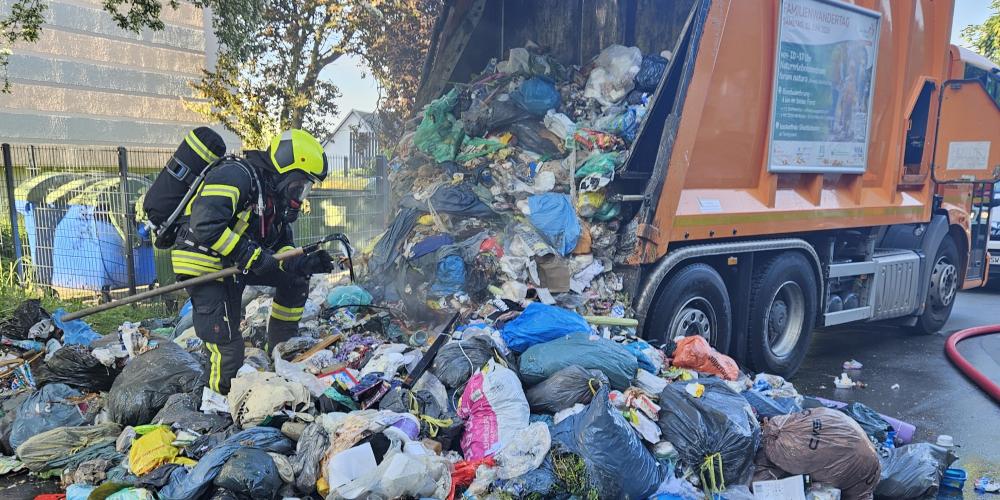Ein Müllfahrzeug hat den Abfall auf eine Straße gekippt, nachdem die Ladung gebrannt hat. Ein Feuerwehrmann durchsucht den Müll nach Glutnestern.