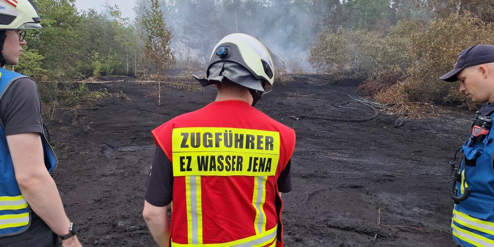 Einsatzkräfte sind von hinten zu sehen vor einer Brandfläche.