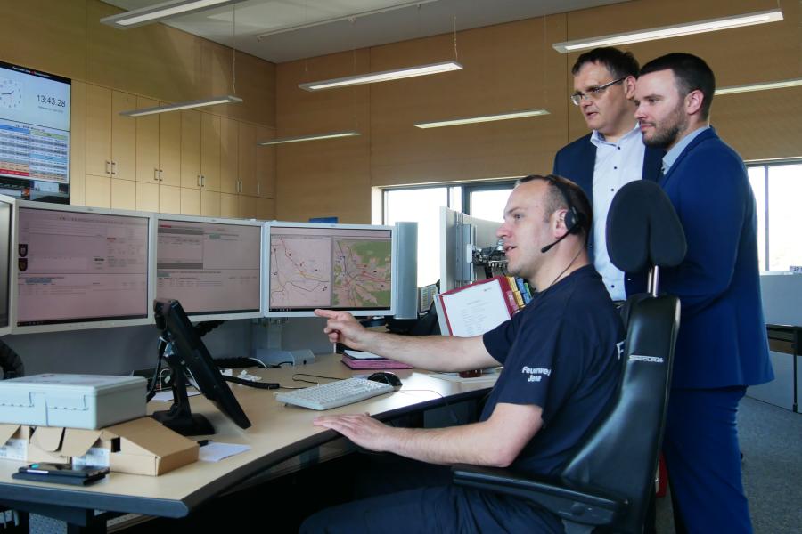 Drei Männer schauen auf den Bildschirm eines Computers in einem großen Raum 