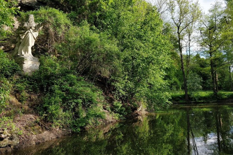 Auf einem Hang an einem Teich steht eine Statue.