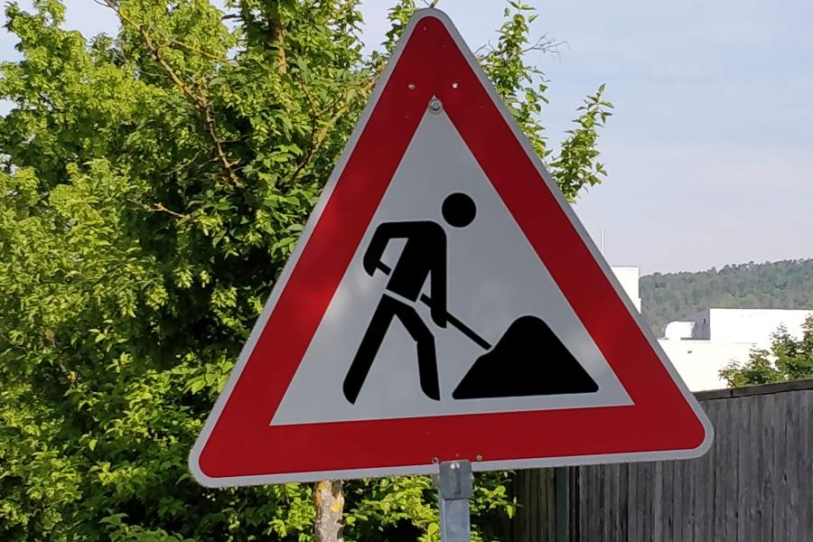 Ein Baustellenschild steht vor einem Baum am Straßenrand.