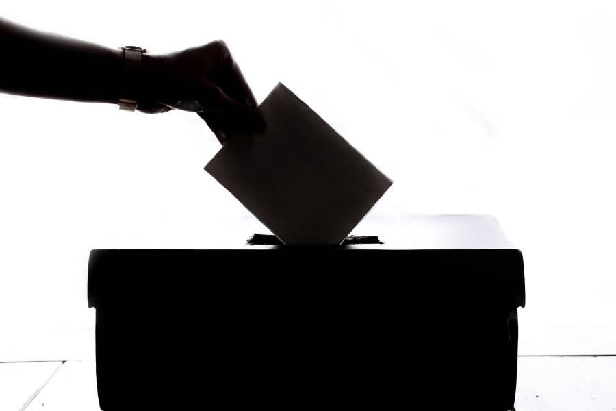 Eine Hand wirft einen Stimmzettel in eine Wahlurne ein.