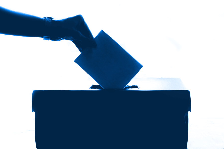 Eine Hand wirft einen Stimmzettel in eine Wahlurne ein.