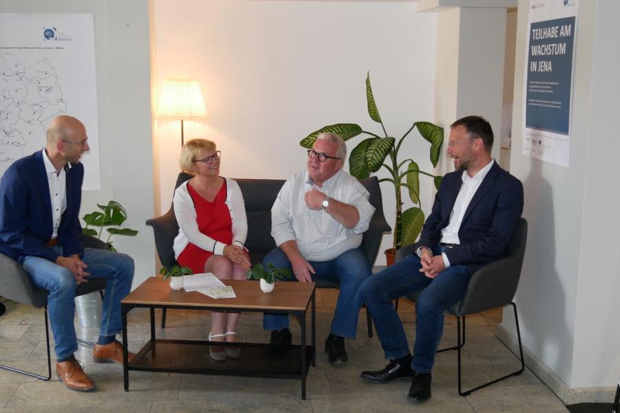 Drei Männer und eine Frau (V.l.: Winfried Röpke (Geschäftsführer Wirtschaftsförderungsgesellschaft Jena mbH), Katja Glybowskaja (Stellvertretende Vorsitzende AWO Regionalverband Mitte-West-Thüringen), Dr. Michael Behling (Behling-Consult) und Oberbürgermeister Dr. Thomas Nitzsche) sitzen im Arebitsladen und unterhalten sich.