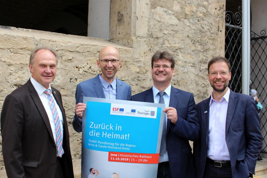 Andreas Heller (Landrat SHK), Wilfried Röpke (Wirtschaftsförderung Jena), Andreas Knuhr (Thüringer Agentur für Fachkräftegewinnung) und Dr. Thomas Nitzsche (Oberbürgermeister Jena) (v.l.n.r.) halten ein Plakat für den Pendlertag vor sich.