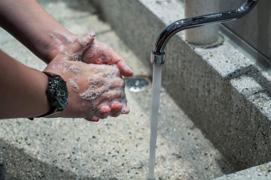 Zwei Hände die sich unter einem Wasserhahn mit laufenden Wasser waschen