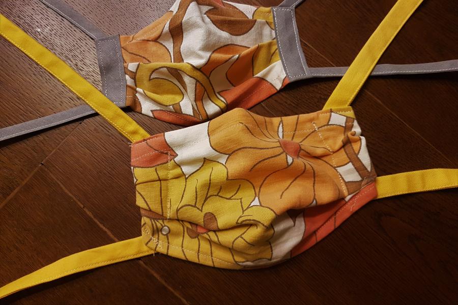 Zwei selbstgenähte Mund-Nasen-Bedeckungen in bunten Farben liegen auf einem Holztisch