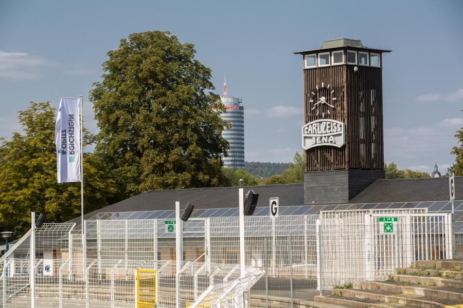 Eine leere Tribüne des Stadions mit dem Jentower im Hintergrund