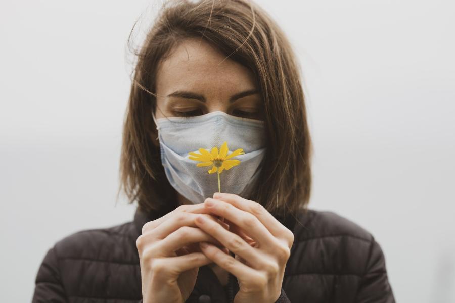 Frau mit Maske hält eine gelbe Blume in den Händen