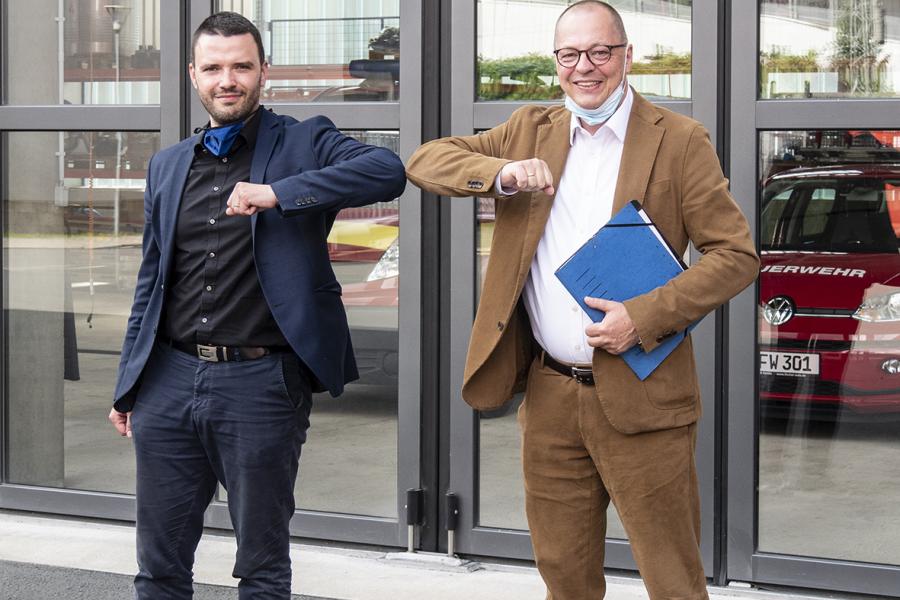 Zwei Männer vor einer Garage stoßen die Ellenbogen zusammen