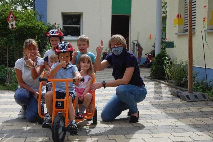 Kinder und Erzieher freuen sich über das neue Dreirad. einige Kinder sitzen schon drauf.