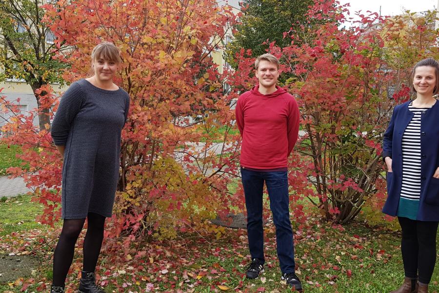 Zwei Frauen und ein Mann stehen im Herbst vor einem Busch.